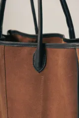 Bolso tipo tote de gamuza color marrón con detalles de bordes y asas en cuero negro.