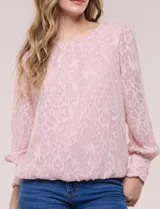 Blusa blanca de organza con textura devoré floral, silueta semiholgada y forro interno. Tiene escote bote, mangas largas abullonadas con transparencias, puños anchos con botones y ruedo elastizado.