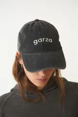 Gorra de gabardina negra con visera curva y aplique metálico plateado con la palabra "garza" en el frente.