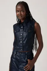 Chaleco azul marino de cuero sintético, con cuello camisero, cierre frontal con botones y bolsillos con solapa en el pecho.