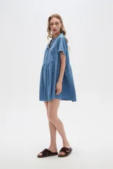Vestido corto camisero de denim celeste, con cuello camisero, mangas cortas y falda acampanada con botones frontales.
