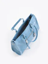 Bandolera de cuero vacuno color celeste con doble asa superior, bolsillo frontal con cierre y tirador largo, y detalle de mosquetón con dije colgante en forma de corazón.