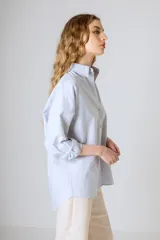 Camisa blanca de corte clásico, con cuello camisero y mangas largas con puños abotonados.