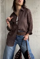 Camisa de rayas verticales marrón y blanca, con calce relajado, mangas largas y cierre frontal con botones.