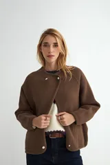 Abrigo corto de paño en color marrón, con cuello redondo, mangas largas y cierre frontal con botones a presión. Presenta un diseño minimalista y elegante.