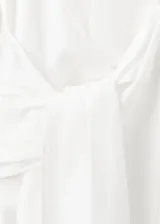 Camisa blanca de manga larga con cuello camisero, cierre frontal de botones y un llamativo detalle de nudo drapeado en el lateral delantero.