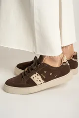 Zapatillas bajas de gamuza color marrón con cordones y suela de goma color crema. Presentan una franja lateral con estampado de vaca y el logo de la marca bordado en el lateral.