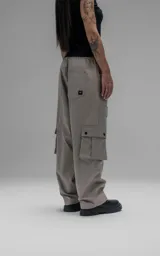 Pantalón cargo de corte oversize y silueta estructurada, confeccionado en microfibra pesada con leve elasticidad. Presenta cintura elástica con cordón de ajuste externo, cierre frontal con botón metálico, bolsillos laterales y bolsillos cargo de gran tamaño con tapa y broches a presión.