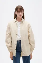 Campera marrón de manga larga confeccionada en algodón, con cuello camisero, cierre frontal con botones a presión y puños elásticos fruncidos.