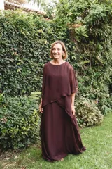 Vestido largo de gasa color bordó, con diseño de capas superpuestas y terminaciones en picos diagonales. Presenta mangas tipo capa que cubren sutilmente los brazos, brindando elegancia y libertad de movimiento.