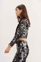 Saco corto de terciopelo negro con estampado floral plateado, cuello cuadrado, mangas largas y aberturas en la zona del abdomen.