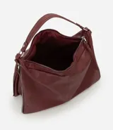 Bolso tipo hobo de gran tamaño en color bordó, confeccionado en poliuretano. Presenta una estructura desestructurada, cierre superior, correas dobles (una de mano y una larga desmontable) y cierres laterales decorativos con tiradores.