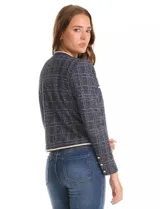 Chaqueta de tejido tweed en tono azul con sutiles destellos de lúrex. Presenta cuello a la base, abertura frontal y bolsillos decorativos. Las mangas largas incluyen detalle de botones metálicos dorados en los puños, y cuenta con vivos a contratono en los bordes.