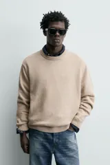 Sweater de punto color beige, de corte regular fit, con cuello redondo y manga larga. Presenta terminaciones en rib en cuello, puños y dobladillo.