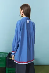 Camisa azul de algodón con detalles de ondas rojas en la solapa del cierre y en los puños, de manga larga y corte oversize.
