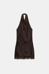 Vestido mini de color marrón oscuro con diseño de cuello halter, espalda descubierta y detalle de pliegues laterales. Presenta un bajo con encaje y abertura, cierre lateral con cremallera oculta y forro interior.