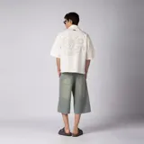 Camisa de manga corta color marfil, confeccionada en 100% algodón con calce boxy, cuello camisero, cierre frontal de botones y diseño con bordado sutil en la parte inferior.