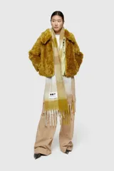 Chaqueta corta de piel sintética peluda, color mostaza/amarillo ocre, con cuello solapa y cierre frontal de cremallera de color amarillo claro.