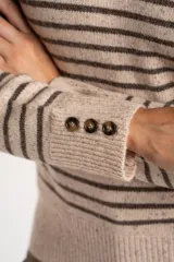 Sweater de lana y nylon, color beige jaspeado con rayas horizontales marrones oscuras. Presenta cuello alto con abertura frontal abotonada con tres botones marrones.
