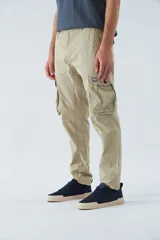 Pantalón cargo color beige, corte slim, con cierre y botón en la cintura, pasacintos, bolsillos cargo con botones y sin puños.