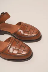 Zapato de cuero color borgoña, con puntera redondeada y diseño trenzado. Presenta una tira sobre el empeine con hebilla metálica negra.