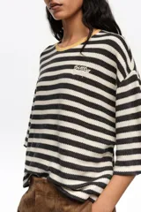 Remera boxy de algodón orgánico con diseño a rayas horizontales en negro y crudo, escote redondo con ribete amarillo, mangas cortas amplias y pequeño bordado en el pecho.