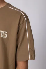 Remera de algodón color blanco con corte regular, cuello redondo y mangas cortas. Presenta detalles de líneas finas negras en los hombros y estampado gráfico frontal con tipografía y logotipos en color negro.