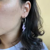 Aros de acero quirúrgico plateado con dije de rayo color lila.