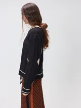 Sweater de punto con diseño de ochos en color verde, cuello redondo con detalle de franja en contraste, y apliques de rombos en las mangas. Presenta un bordado con la letra M en el pecho.