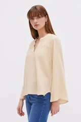Blusa blanca de viscosa con detalles de broderie en los hombros, cuello en V y mangas largas holgadas.