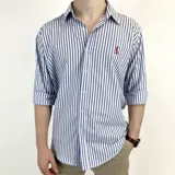 Camisa de vestir a rayas verticales azules y blancas, de corte clásico, con cuello italiano y mangas largas con puños abotonados. Presenta logo bordado en el pecho. Marca Duxon.