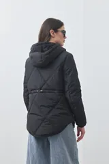 Campera puffer negra con diseño acolchado, capucha integrada y cierre frontal con botones a presión. Presenta puños elásticos y costuras decorativas en el frente.
