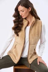 Chaleco de tejido tipo sherpa en color beige, con cierre frontal completo y detalles de terminación en cuero sintético. Cuenta con bolsillos laterales con cierre y un diseño sin mangas que permite libertad de movimiento.