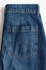 Jean de corte wide leg tiro alto, confeccionado en denim azul con efecto desgastado. Presenta diseño de cinco bolsillos, detalles trenzados a los lados y dobladillo ancho pespunteado.
