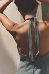 Vestido corto de denim con escote halter y cuello en pico, tirantes cruzados para atar en el cuello y falda acampanada con pliegues.