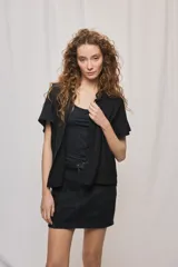 Camisa negra de manga corta, silueta amplia y tejido liviano con textura. Presenta cuello mao, cierre frontal con botones y diseño fluido.