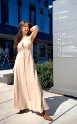 Vestido largo color beige, con breteles finos, escote con cordones cruzados y falda acampanada.