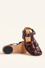 Sandalias de cuero color negro con diseño de tiras cruzadas tipo huarache, tira ajustable con hebilla metálica en el empeine y taco cilíndrico de madera.