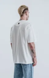 Remera oversize de algodón premium color blanco tiza, con cuello redondo rib al tono y hombros caídos.
