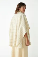 Ruana corta de lana virgen color beige con diseño a cuadros finos oscuros y bolsillos frontales aplicados.