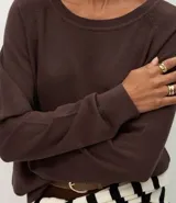 Suéter de punto color marrón chocolate, con cuello redondo y mangas largas con puños acanalados. Presenta un diseño básico y versátil de corte recto.