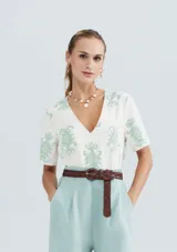 Blusa color beige con estampado de hojas color verde agua, escote en V y mangas cortas.