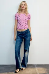 Top de punto fino color rosado, con cuello redondo, manga corta y estampado de lazos morados distribuidos en un patrón de rombos.
