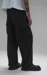Pantalón cargo de estilo técnico en color negro, confeccionado en textil memory con acabado sutilmente brillante. Presenta una silueta oversize, cinturón regulable integrado con hebilla de encastre, dos bolsillos laterales, dos bolsillos cargo de gran tamaño y un bolsillo trasero.