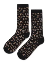 Medias largas de algodón en color negro con estampado de motivos western en tono beige, incluyendo botas, revólveres, herraduras y cráneos de toro.