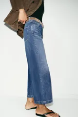 Jeans de tiro alto con pernera ancha y corte cropped. Presenta diseño de cinco bolsillos, cierre frontal con cremallera y botón, e incluye un cinturón oscuro con hebilla metálica.