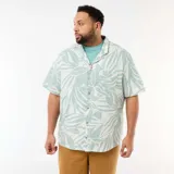 Camisa de manga corta verde claro y blanca con estampado tropical de hojas, cuello camisero, cierre frontal con botones y bolsillo aplicado en el pecho.