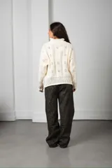 Cárdigan de punto color beige con textura calada de motivos florales, cuello alto, cierre frontal con botones y mangas largas con terminaciones acanaladas.
