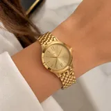 Reloj analógico Michael Kors con caja y malla de eslabones en acero inoxidable color dorado. Presenta una esfera minimalista con números romanos en las posiciones de las 12 y las 6, y manecillas finas.