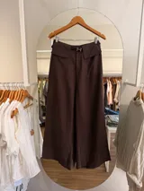 Pantalón de tiro alto color marrón, de corte fluido y silueta amplia, con bolsillos delanteros con solapa y cinturón delgado incorporado con hebilla metálica.